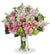 A floral arrangement featuring green hydrangea, pink roses, white roses, pink spray roses, light pink alstroemeria, pink lisianthus, and white stock in various shades of pink, green, and white tones, presented in a clear glass vase.