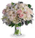 A bouquet of white, crème, and light pink roses with hydrangea and lilies in a clear vase.